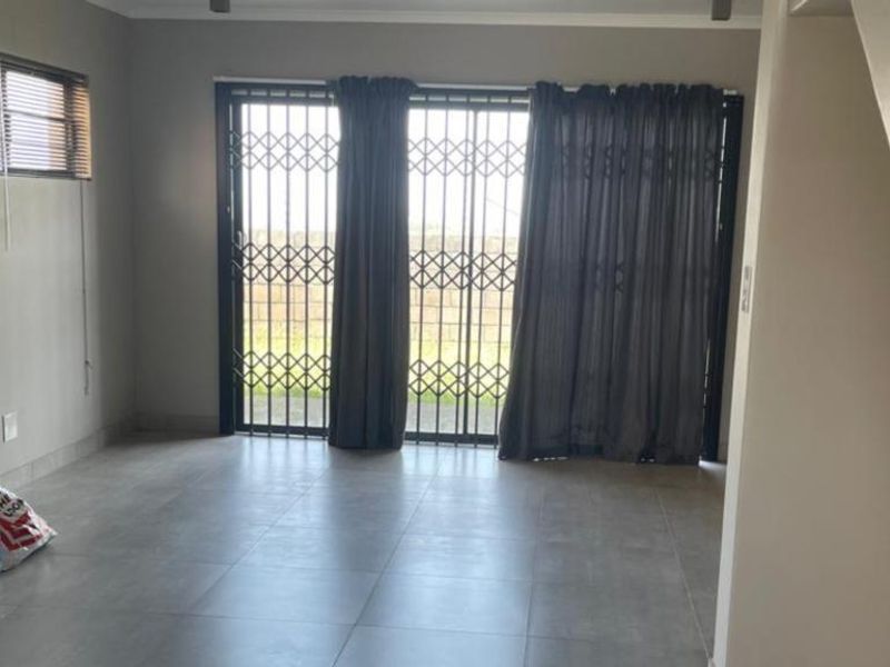 An open-plan living area featuring large format floor tiles, a sliding door with security gate, and access to an adjacent staircase.