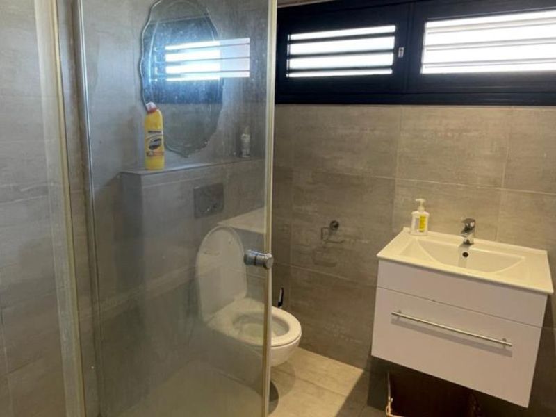 Modern bathroom featuring a wall-mounted toilet, glass shower enclosure, and a sleek vanity basin with tiled finishes throughout.