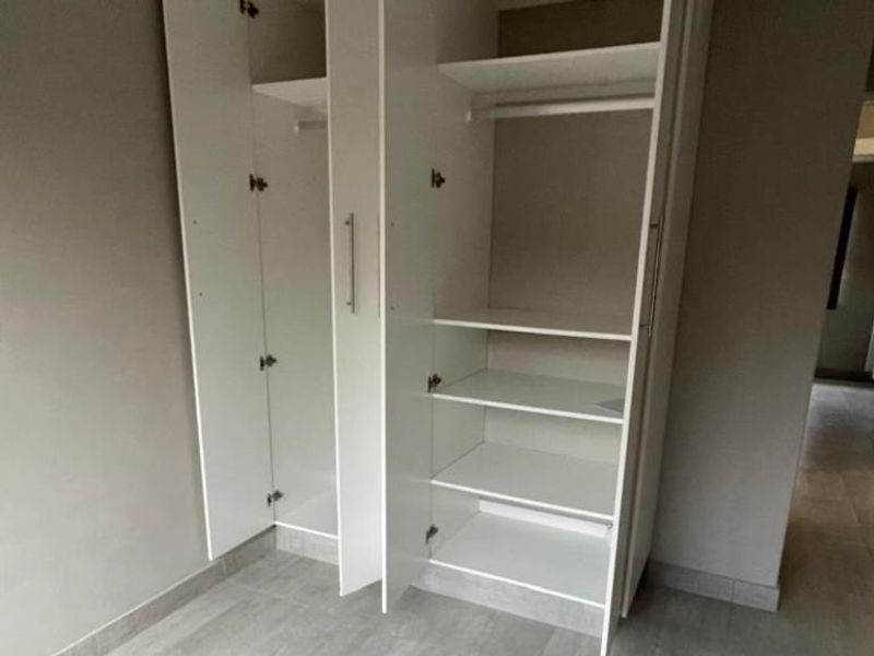 A clean, empty bedroom featuring modern built-in cupboards and neutral tiled flooring, offering a blank canvas for personalization.