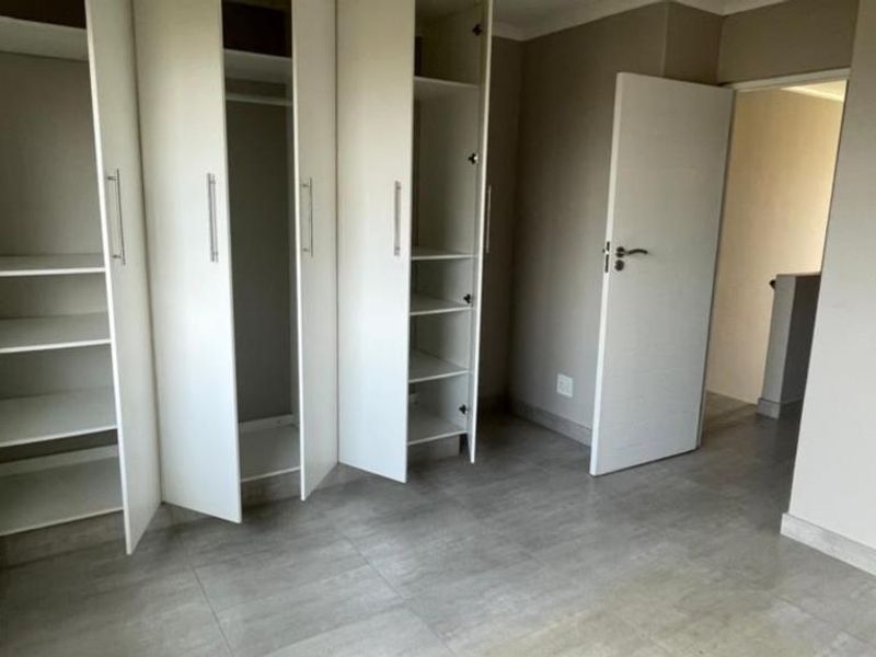 A clean, empty bedroom featuring neutral wall tones, modern grey floor tiles, and ample built-in cupboard storage space.