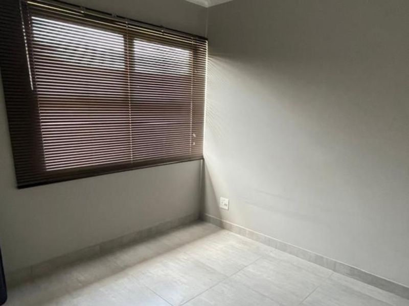 A bright, empty bedroom featuring neutral tiled flooring, clean walls, and fitted venetian blinds, offering a versatile space ready for personalization.