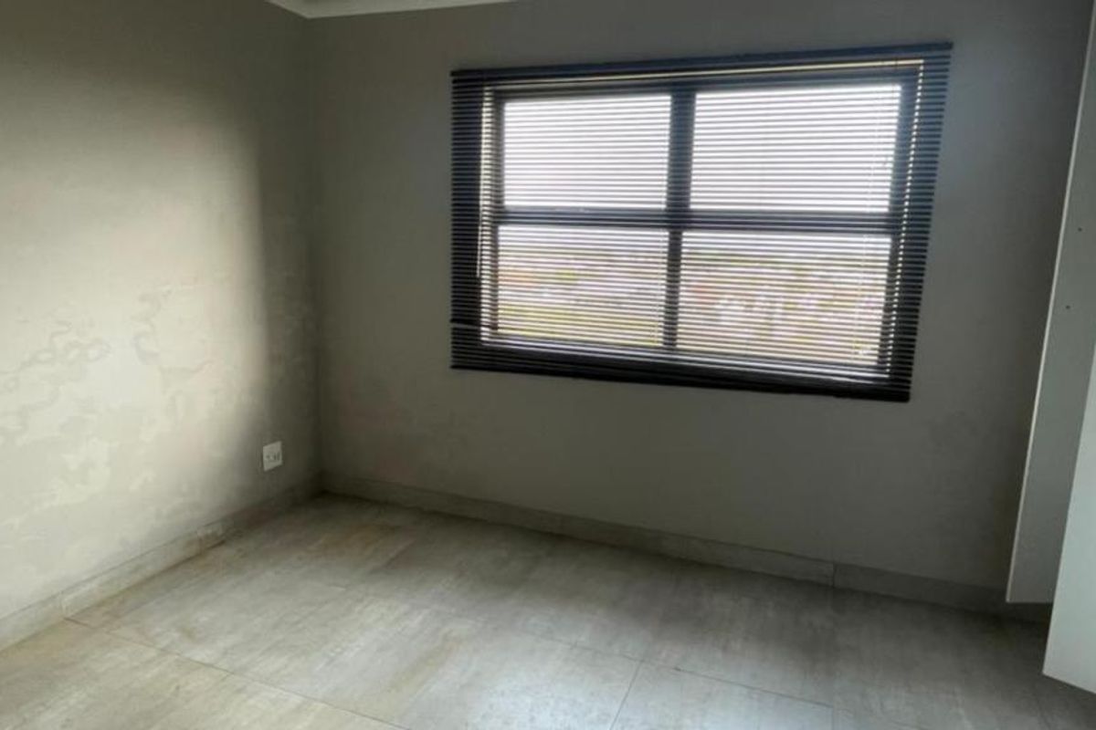 An empty bedroom featuring tiled flooring, built-in cupboards, and venetian blinds, requiring minor wall repairs and repainting to refresh the space.