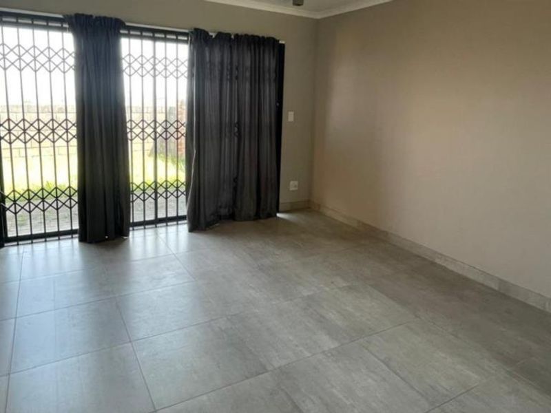 A spacious, empty living area featuring neutral tiled flooring and a sliding glass door with an integrated security gate leading to the exterior.