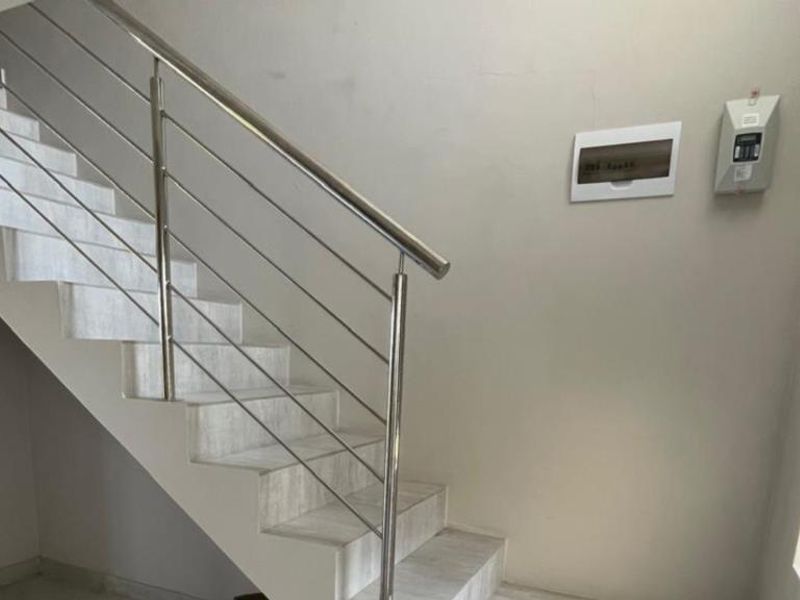 A bright hallway featuring a modern staircase with a stainless steel balustrade, tiled steps, and a wall-mounted electrical distribution board.