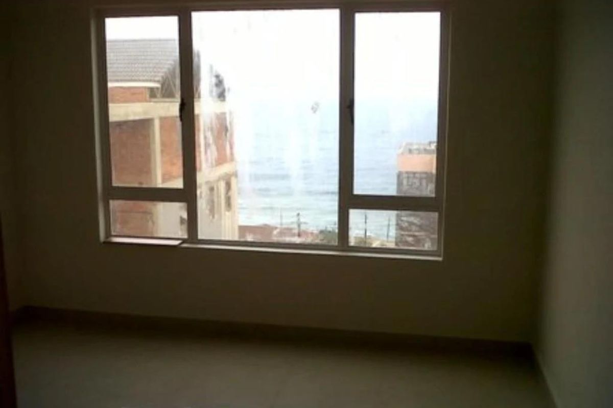An empty bedroom featuring large windows with a view of the surrounding neighborhood and distant sea.
