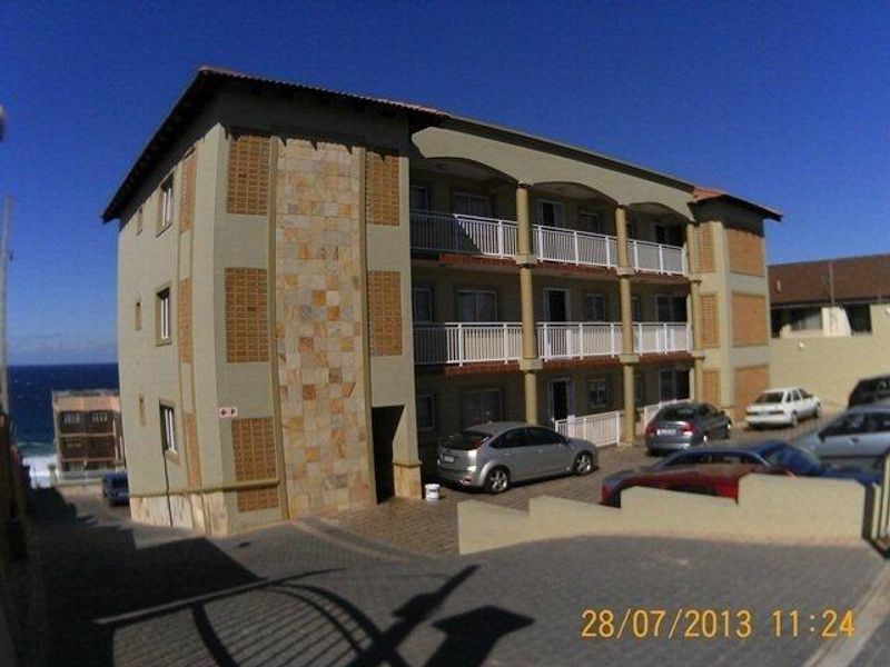 Exterior view of a multi-story apartment building featuring stone cladding accents, private balconies, and paved parking area.