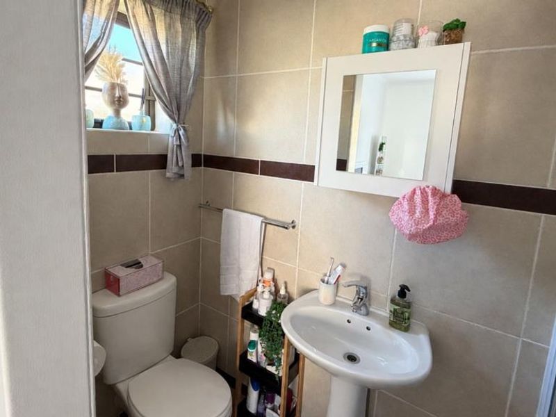 A clean, empty bedroom featuring neutral tiled flooring, a window with security bars, and a built-in cupboard.