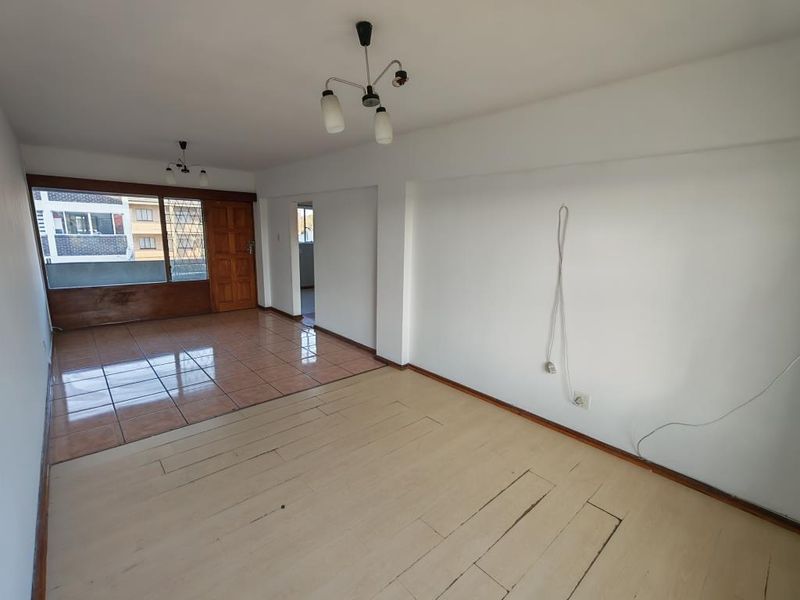 An empty living room featuring a combination of ceramic tile and wooden flooring, with large windows and access to an adjacent area.