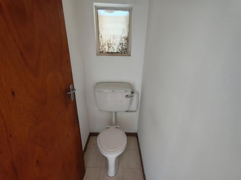 A small, dated bathroom featuring a standard toilet and a small window. The space requires cosmetic updates and repairs to finishes.