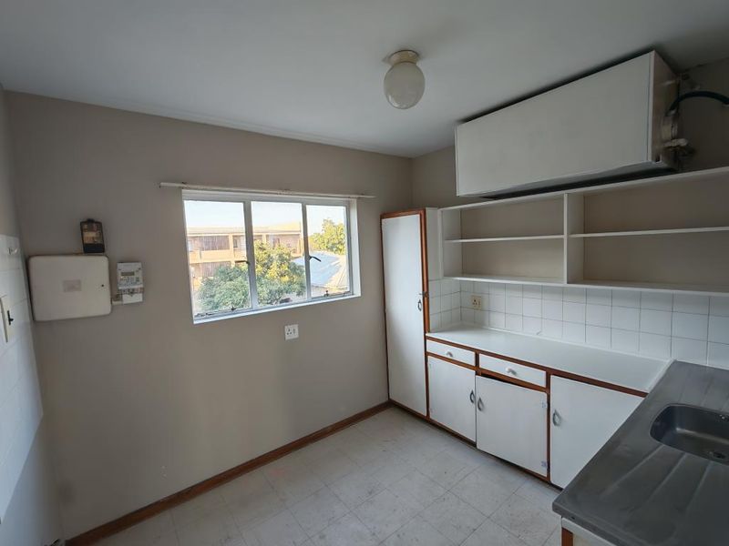 A functional, empty kitchen featuring built-in cabinetry, open shelving, a stainless steel sink, and a tiled backsplash, offering potential for modernization.