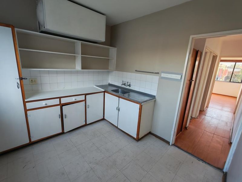 A dated kitchen featuring original built-in cabinetry, a stainless steel sink, and tiled backsplash, offering a blank canvas for modern renovation.