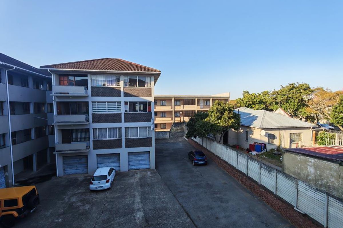 Exterior view of the apartment complex rear facade, featuring a concrete driveway, garage access, and perimeter boundary wall.