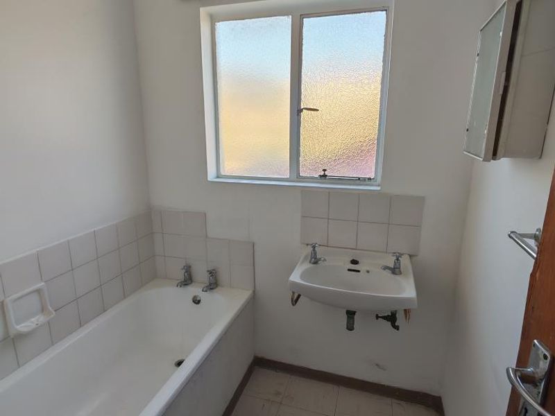 A basic, dated bathroom featuring a bathtub, wall-mounted basin, and tiled finishes, requiring cosmetic updates to improve its overall condition and appeal.