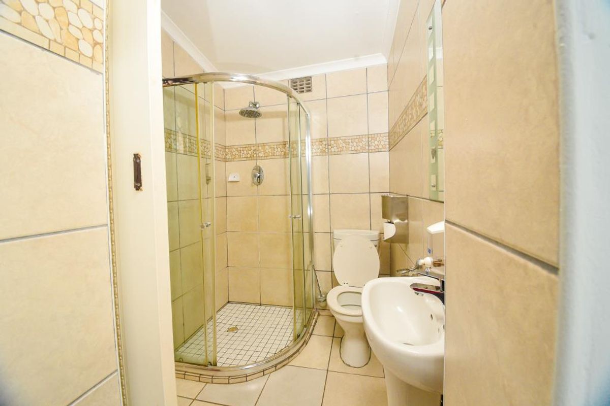 A compact bathroom featuring a corner glass shower enclosure, pedestal basin, and toilet with neutral wall and floor tiling.