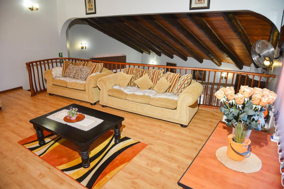 A spacious mezzanine living area featuring exposed timber beam ceilings, wooden flooring, and a decorative wooden balustrade overlooking the lower level.