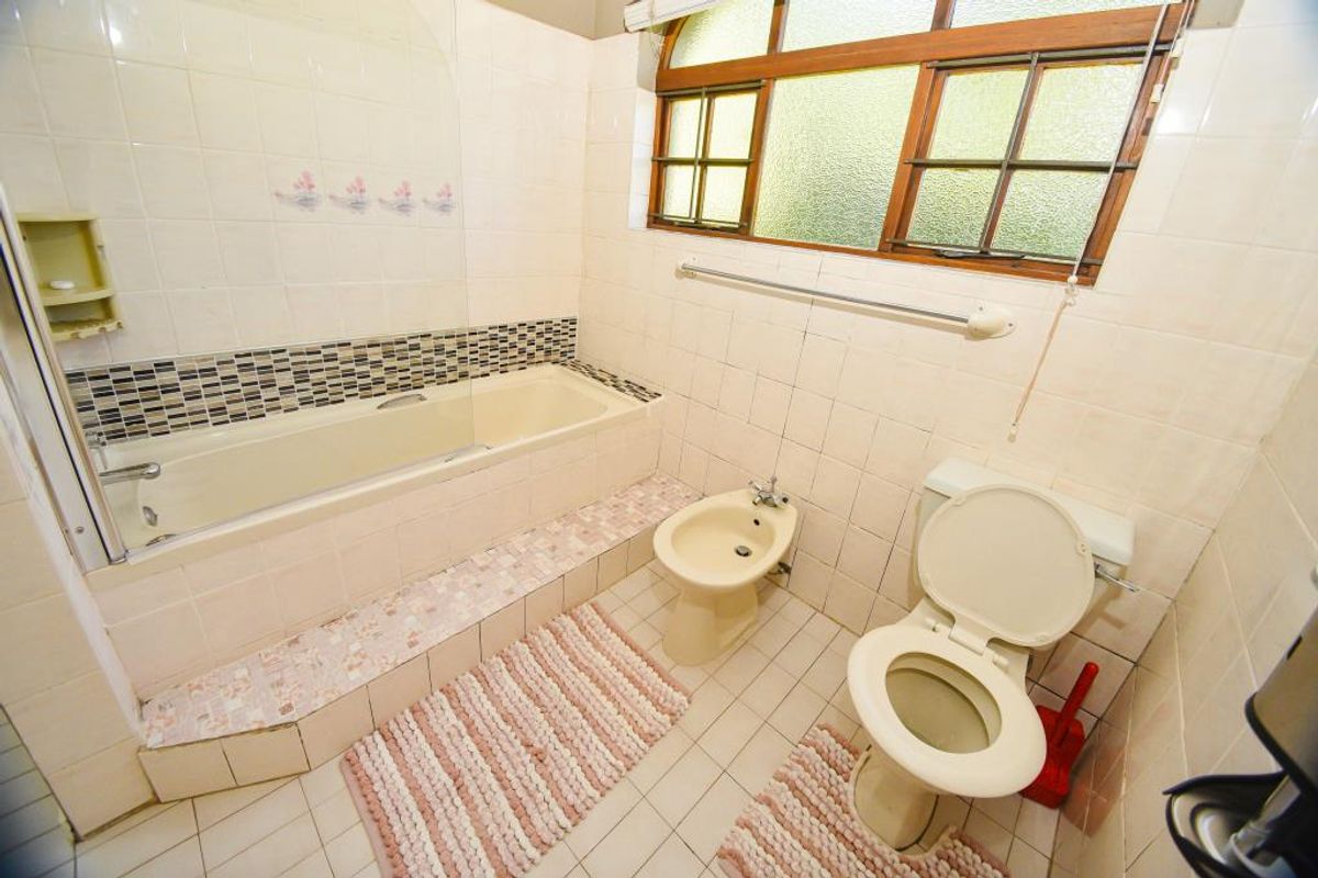 A dated bathroom featuring a built-in bathtub with shower screen, toilet, and bidet, finished with original wall and floor tiling.