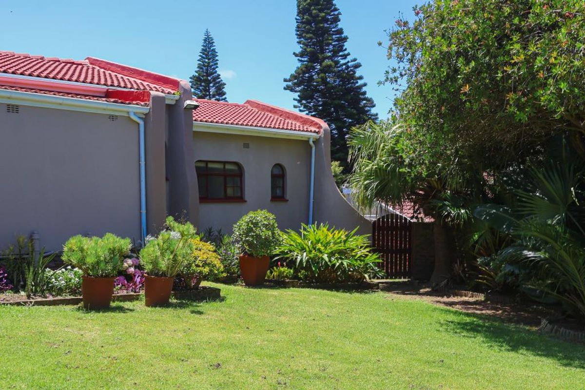 A view of the rear exterior of the apartment building, featuring a well-maintained lawn, established garden beds, and a private gated access point.