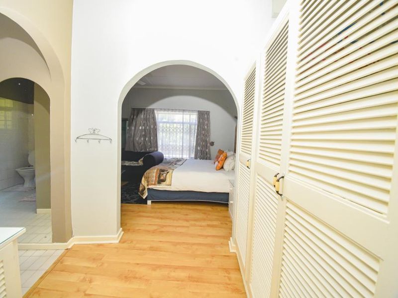 A bedroom suite featuring arched doorways, built-in louvered wardrobe cabinetry, and laminate flooring, with an adjoining bathroom visible through the archway.
