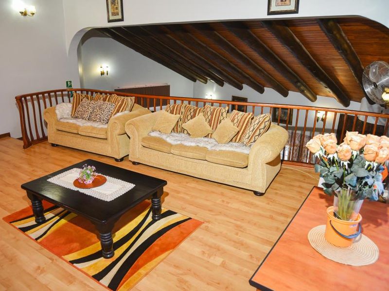 A spacious mezzanine living area featuring exposed timber beam ceilings, wooden flooring, and a decorative wooden balustrade overlooking the lower level.