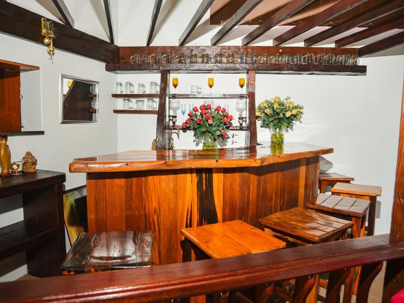 A rustic home bar area featuring a custom timber bar counter, integrated shelving, and exposed wooden ceiling beams.
