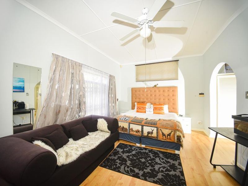 A spacious bedroom featuring laminate flooring, a ceiling fan, and arched architectural details, providing a comfortable and functional living space.