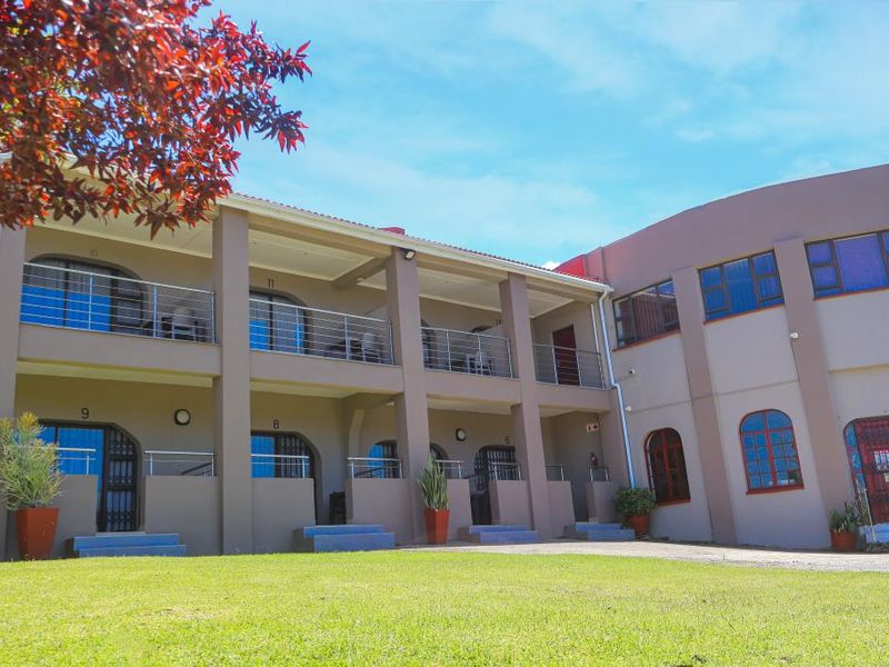 Exterior view of a multi-level apartment complex featuring balconies with stainless steel railings and a well-maintained lawn area.