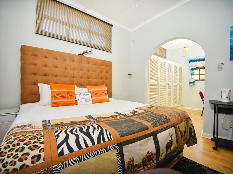 A bedroom featuring a built-in arched doorway leading to a dressing area with fitted louvered wardrobes and laminate flooring.