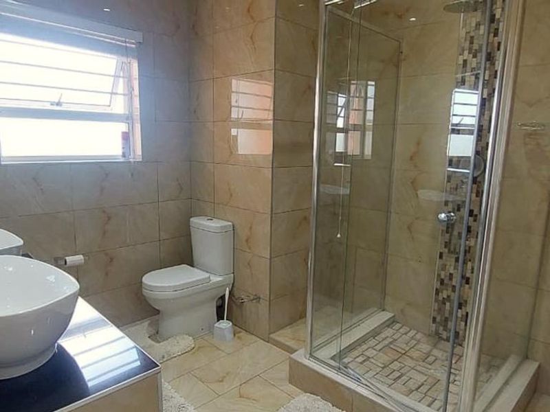 Modern bathroom featuring a double vanity with vessel sinks, a glass-enclosed shower, and floor-to-ceiling tiled finishes.