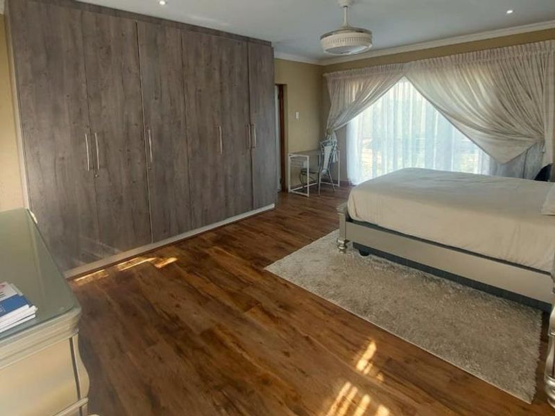 Spacious bedroom featuring extensive built-in cupboards, warm laminate flooring, and a sliding glass door providing natural light and access to the outdoors.