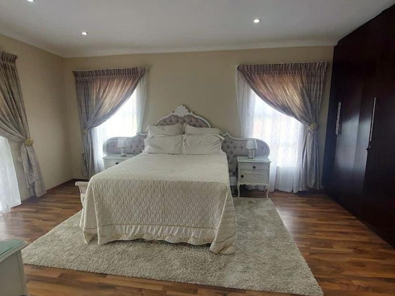Spacious bedroom featuring dark wood built-in cupboards, warm laminate flooring, and recessed downlighting, creating a comfortable and functional sleeping area.