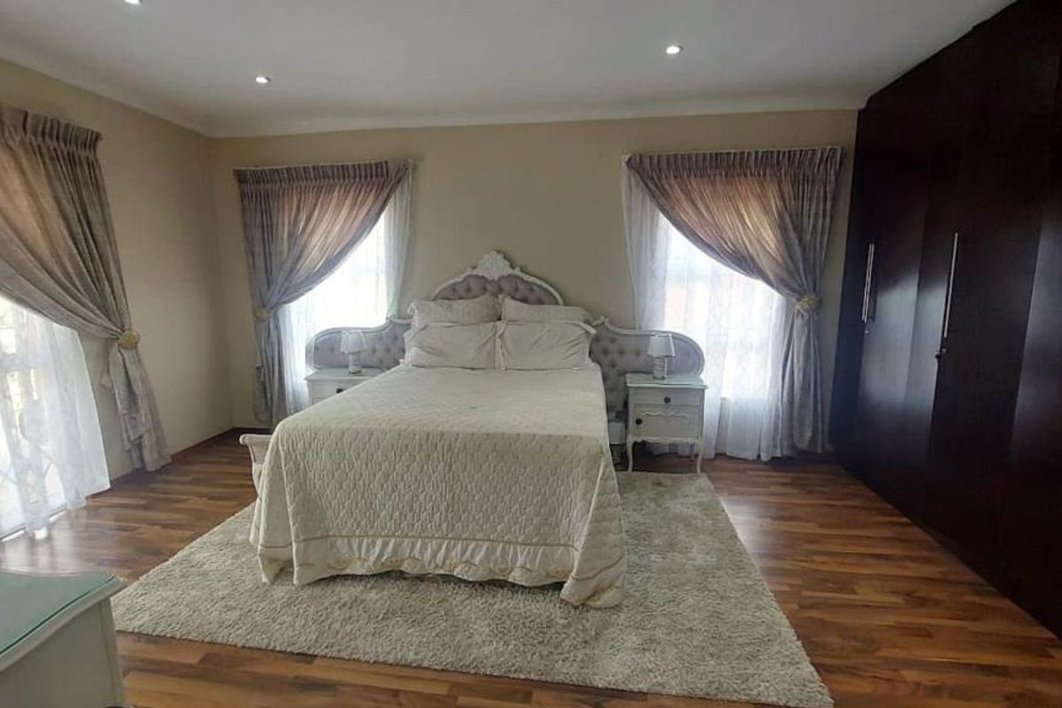 Spacious bedroom featuring dark wood built-in cupboards, warm laminate flooring, and recessed downlighting, creating a comfortable and functional sleeping area.