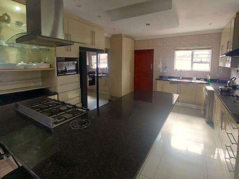 Spacious kitchen featuring granite countertops, a central island with a gas hob, built-in oven, and ample cabinetry with integrated lighting.