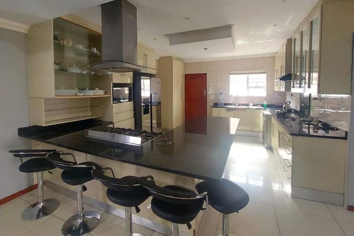 Spacious kitchen featuring a large central island with a built-in hob, granite countertops, ample cabinetry, and modern stainless steel extractor fan.