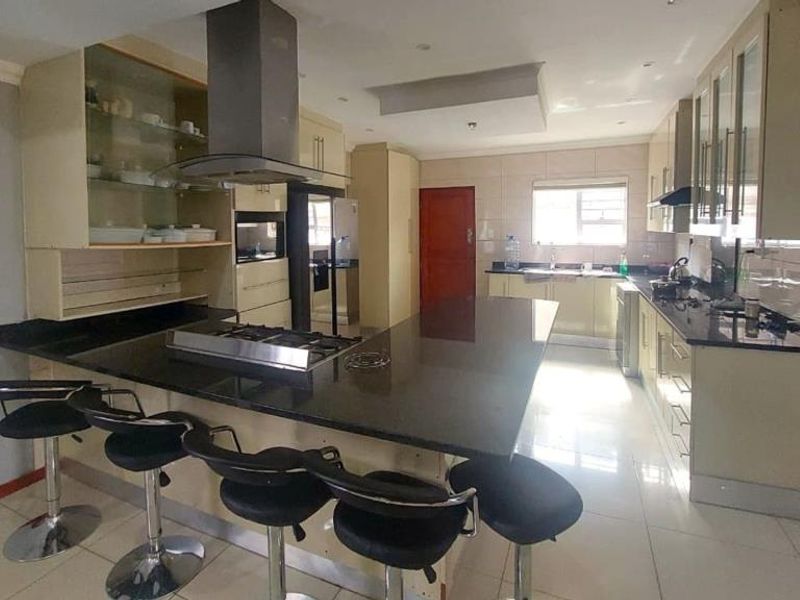 Spacious kitchen featuring a large central island with a built-in hob, granite countertops, ample cabinetry, and modern stainless steel extractor fan.