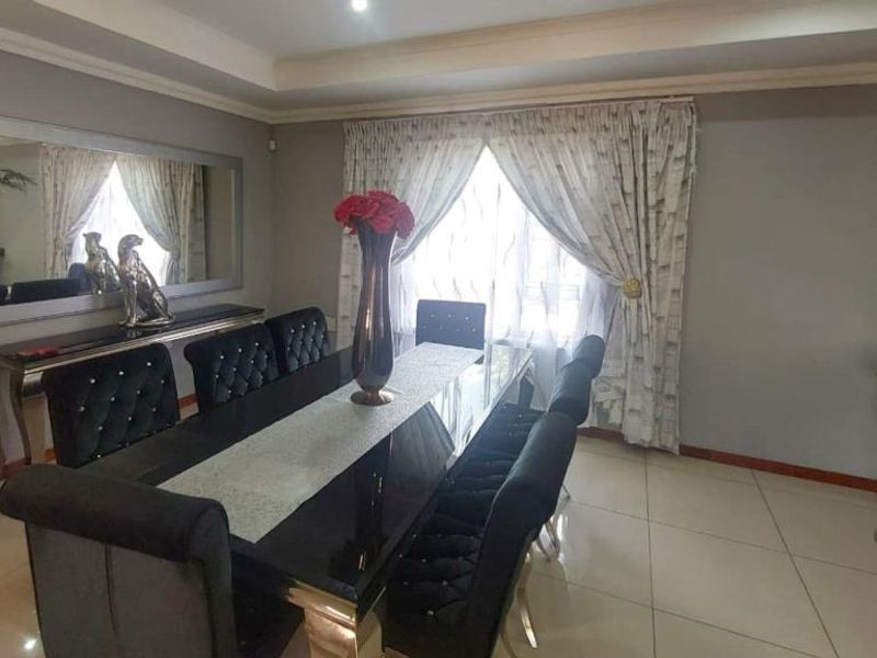A well-maintained dining room featuring tiled flooring, a recessed ceiling with cove lighting, and an adjacent built-in kitchen counter area.