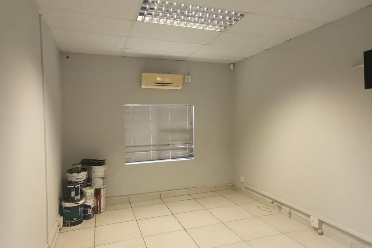 A functional commercial office space featuring tiled flooring, a suspended ceiling with recessed lighting, and a wall-mounted air conditioning unit.