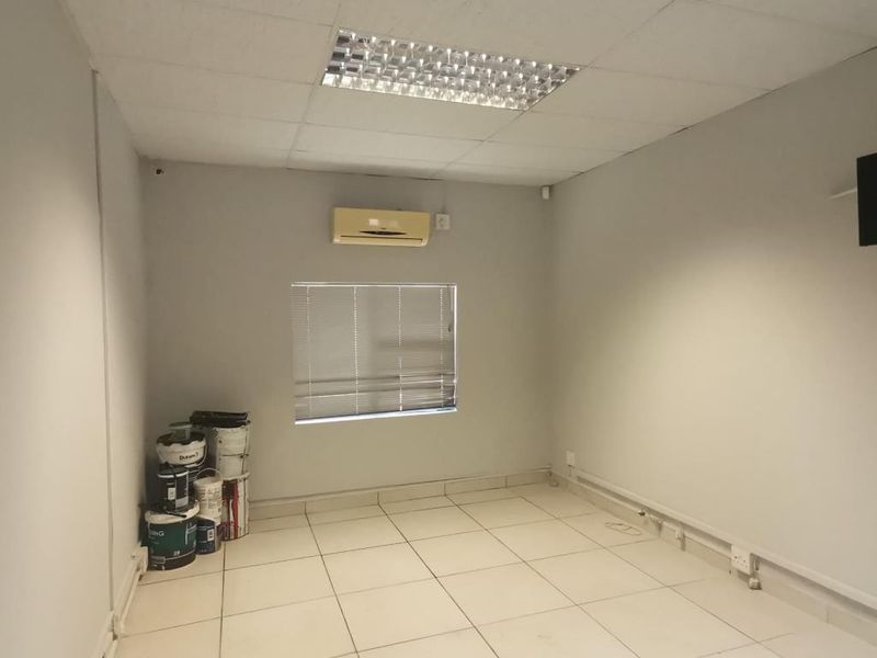A functional commercial office space featuring tiled flooring, a suspended ceiling with recessed lighting, and a wall-mounted air conditioning unit.