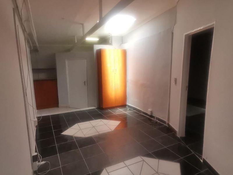 An interior commercial space featuring dark tiled flooring, built-in cabinetry, and exposed structural elements, requiring cosmetic updates and electrical finishing.