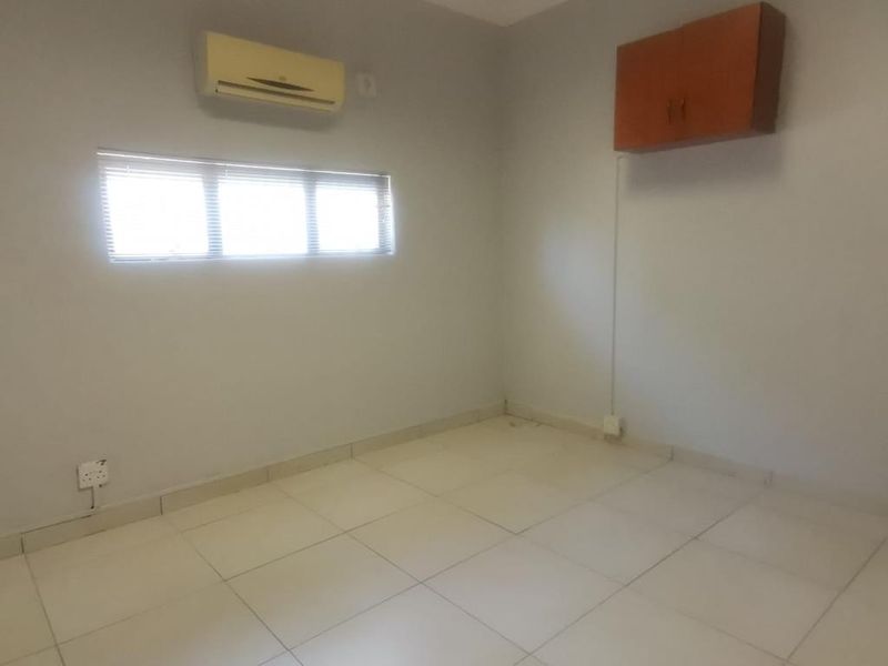 A vacant commercial office space featuring tiled flooring, a wall-mounted storage cabinet, and a wall-mounted air conditioning unit.