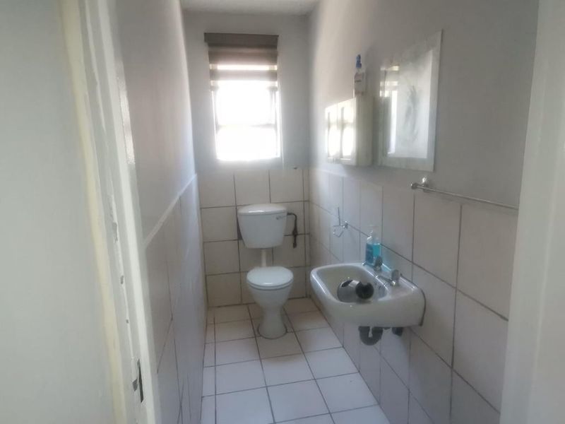 A functional commercial restroom featuring a wall-mounted basin, standard toilet, and tiled walls and flooring with natural light from a window.
