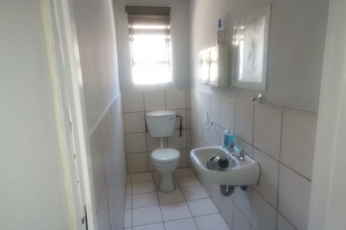 A functional commercial restroom featuring a wall-mounted basin, standard toilet, and tiled walls and flooring with natural light from a window.