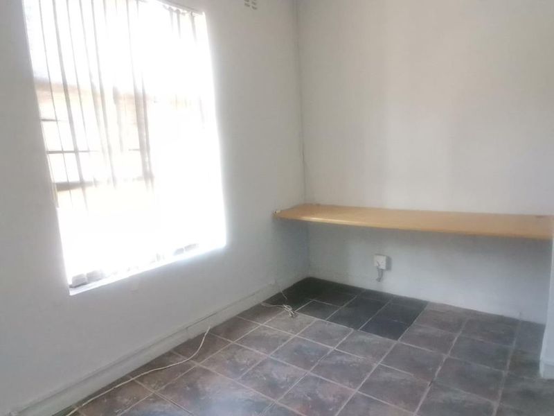 A functional office space featuring tiled flooring, a built-in desk, and a wall-mounted air conditioning unit.