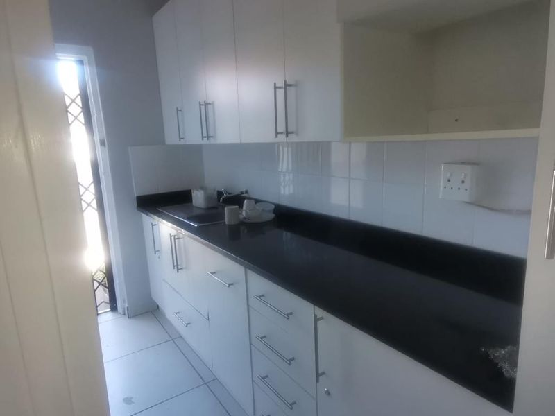 A compact, modern kitchen featuring white cabinetry, dark countertops, and tiled flooring, providing a clean and functional workspace.