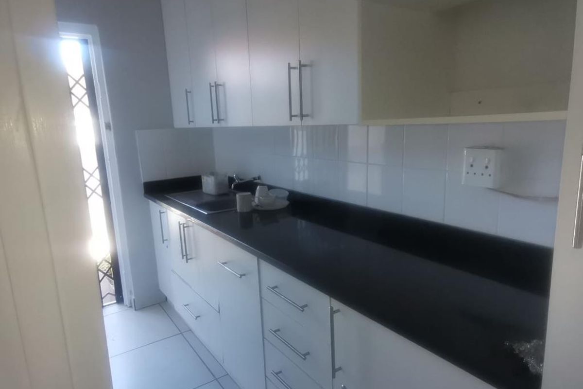 A compact, modern kitchen featuring white cabinetry, dark countertops, and tiled flooring, providing a clean and functional workspace.