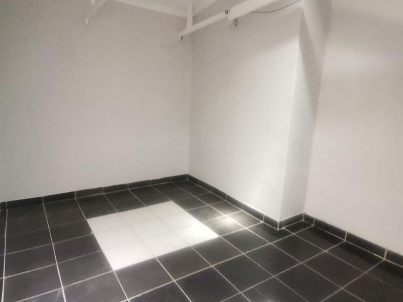 A vacant, neutral-toned utility space featuring dark floor tiles with a contrasting white tiled inlay and exposed ceiling beams.