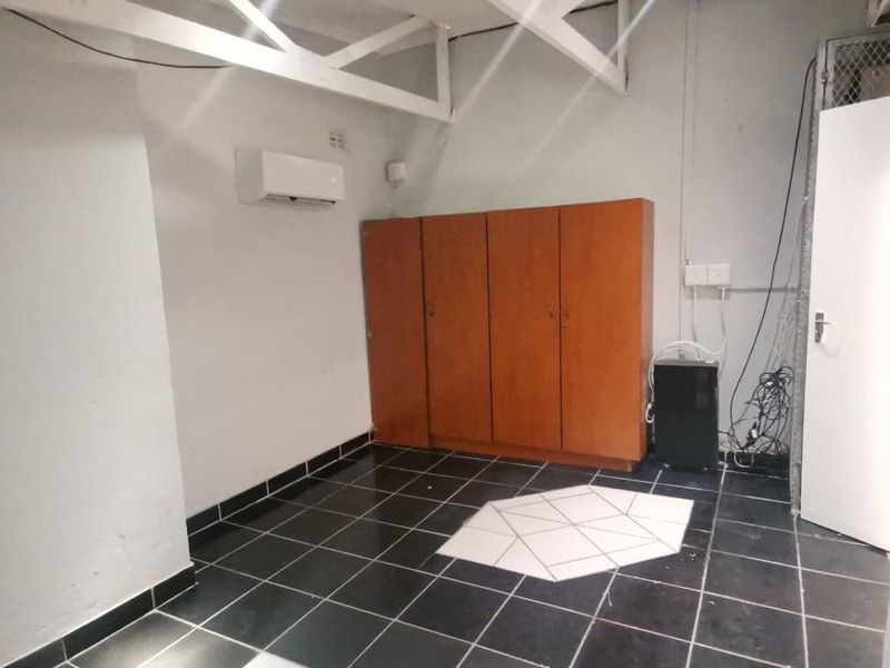 A functional commercial office space featuring tiled flooring, wall-mounted air conditioning unit, and built-in storage cabinetry.