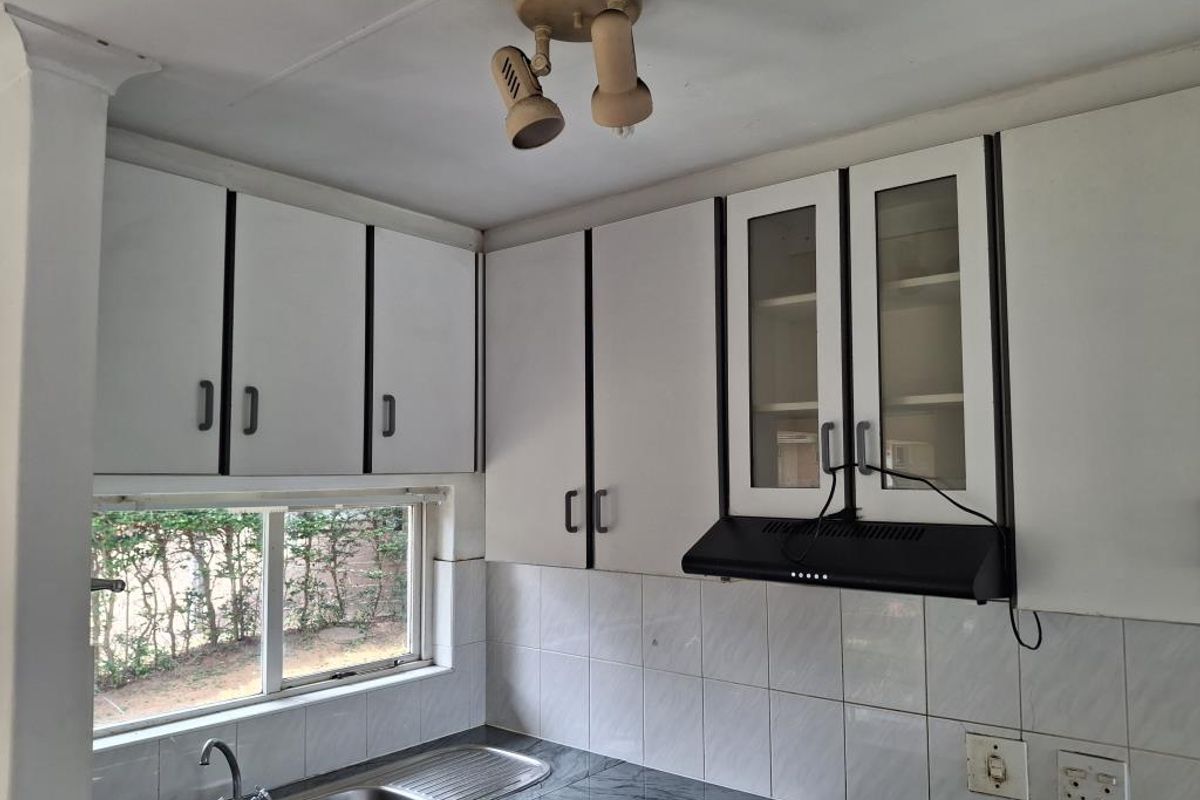 A functional kitchen featuring white cabinetry, a stainless steel sink, tiled backsplash, and a built-in extractor fan.