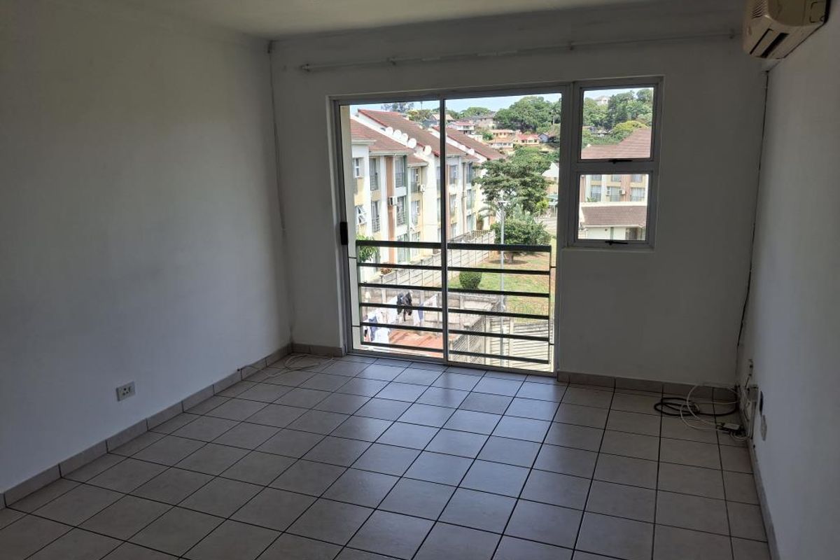An empty living room featuring tiled flooring, a wall-mounted air conditioning unit, and large sliding glass doors leading to a balcony.