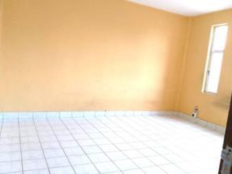 An empty bedroom featuring tiled flooring and a single window, providing a blank canvas for potential interior design updates.