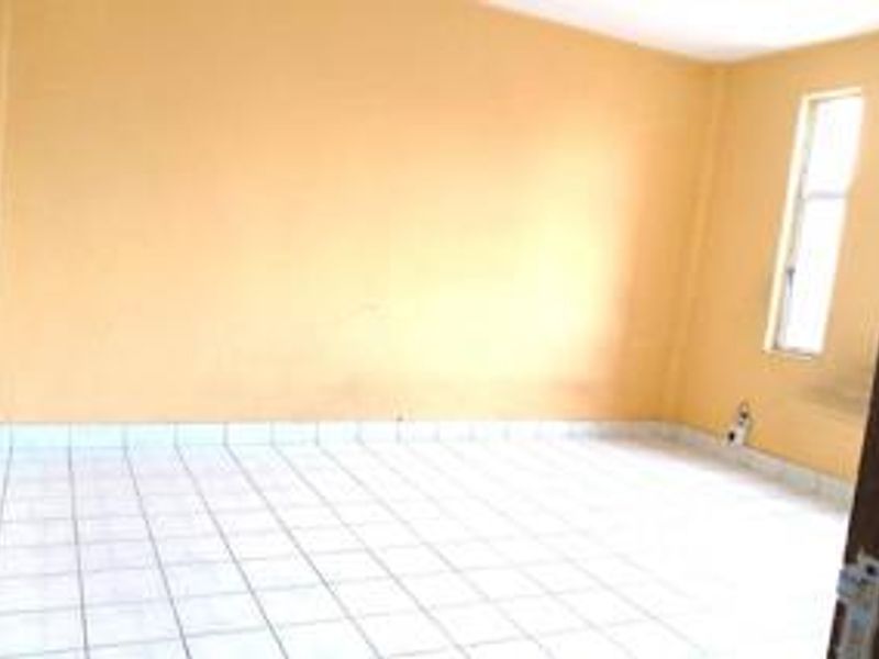 An empty bedroom featuring tiled flooring and a single window, providing a blank canvas for personalization.